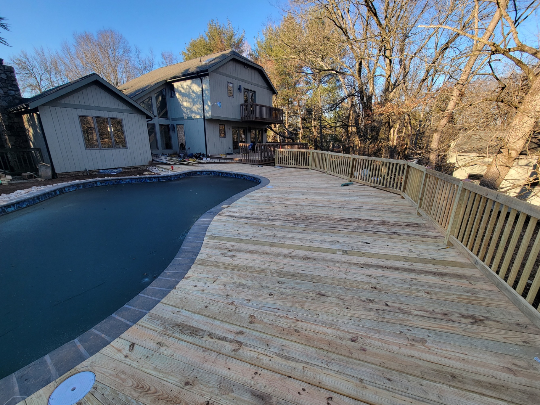 Wide pool deck along curved pool with pressure-treated railings